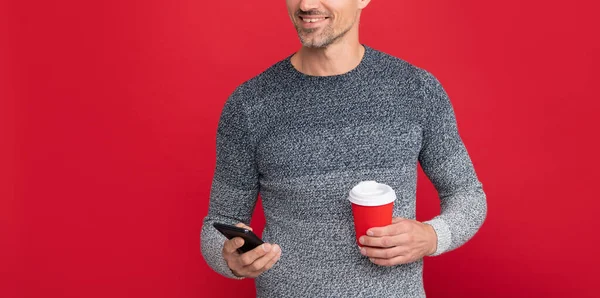 Boldog jóképű férfi visel pulóver tartsa telefon és kávé csésze, kommunikáció — Stock Fotó