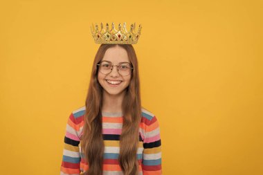 Gözlüklü mutlu çocuk sarı arka planda kraliçe tacı takıyor, zafer