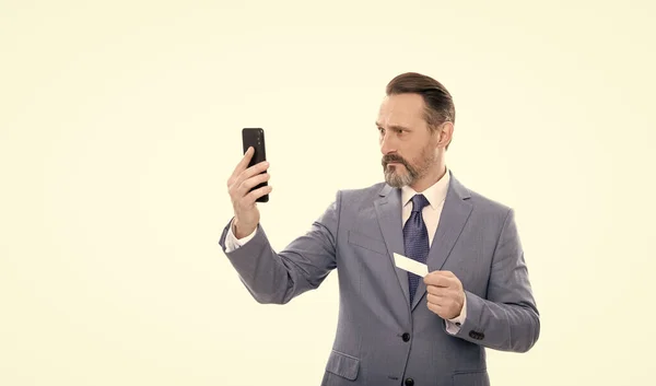 Серйозний зрілий бос у костюмі тримає кредитну картку і телефон ізольовано на білому, селфі — стокове фото