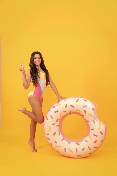 Щаслива пляжна дитина в купальнику з пончиком надувний кільце на жовтому фоні, купальник . — стокове фото