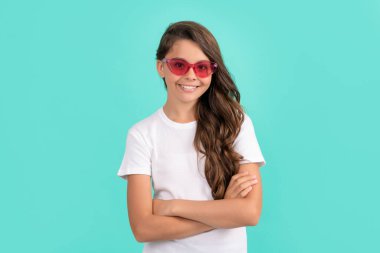 Mutlu genç kız güneş gözlüklü uzun kıvırcık saçlı mavi arka planda, moda