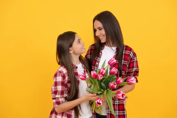 Happy mother and girl with tulip flowers on yellow background — Fotografia de Stock