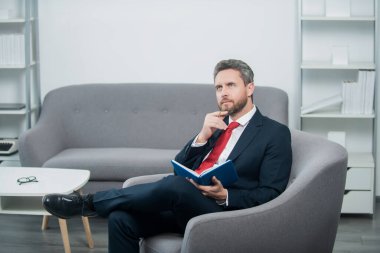 mature businessman in suit sit in reading office making notes in notebook