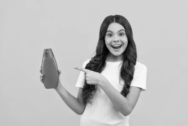 Erstaunt teen girl mit langen haaren, die finger auf shampoo-flasche, promotion — Stockfoto
