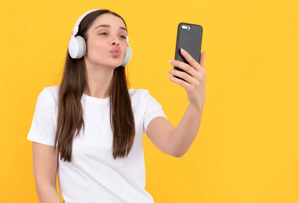 Young girl listen music in headphones hold phone on yellow background, communication — Photo