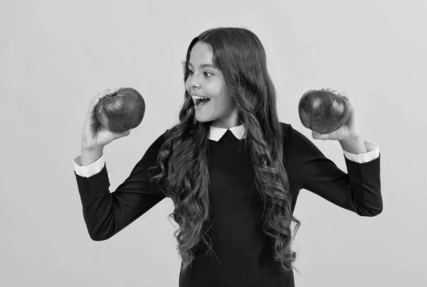 Щаслива дівчина-підліток вибирає червоне вітамінне яблуко для обіду на жовтому фоні, вибір — стокове фото