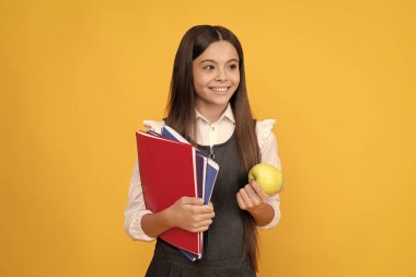 Elma ve kitaplarla okula dönen mutlu kız çocuğu. Sarı arka plan, bilgi günü.