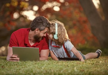 Mutlu baba ve oğul ailesi ders için dizüstü bilgisayar kullanıyor. Kulaklıklarda müzik dinliyor, ebeveynlik yapıyor..