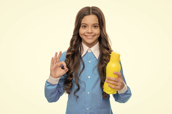 Happy girl show OK sign holding yellow plastic drinking water bottle, healthy habits