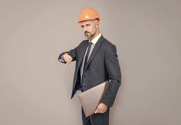 Zakenman in gebouw helm hold laptop controleren tijd, op schema — Stockfoto