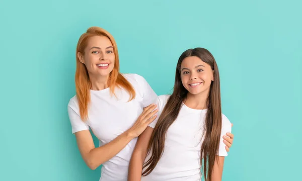 Liefdevolle vrolijke moeder omarmen dochter in witte shirts op blauwe achtergrond, geluk — Stockfoto