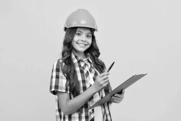 Cheerful kid in construction helmet making notes in clipboard, taking notes — Stockfoto