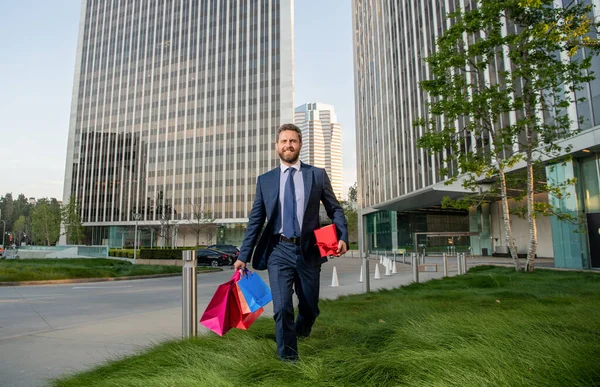 Takım elbiseli tam teşekküllü girişimci elinde alışveriş çantası ve hediye kutusu, yıldönümü hediyesi..