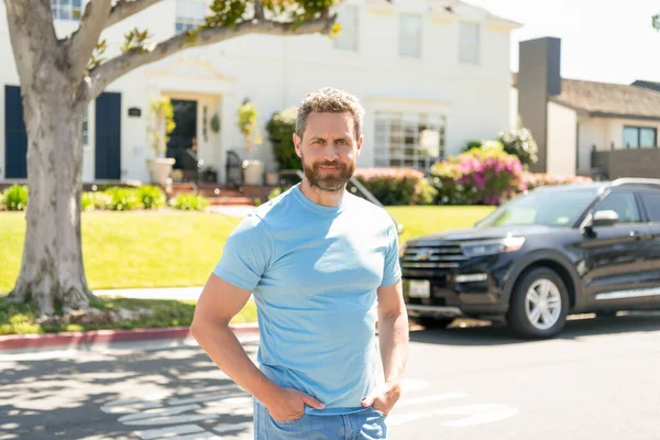 smiling dealer man standing next to the car and new house