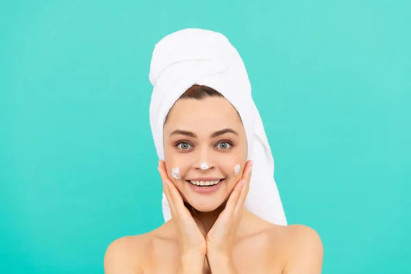 Menina feliz aplicando creme facial no fundo azul — Fotografia de Stock