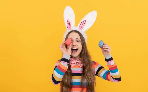 Happy child in bunny ears and bow tie hold easter eggs on yellow background — Zdjęcie stockowe