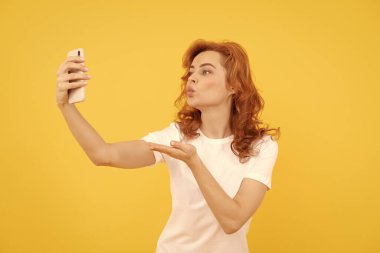 Gadget bağımlısı. Selfie kız blogcu sarı arka plan. Kadın akıllı telefona el öpücüğü veriyor.