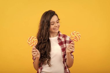 Uzun kıvırcık saçlı hippi çocuk lolipopu tutuyor. Çubukta şeker. Karamelli şeker dükkanı.
