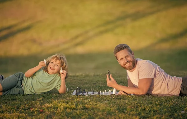 Papa et gamin jouent au jeu de logique. père et fils jouant aux échecs sur l'herbe dans le parc. fête des pères. — Photo