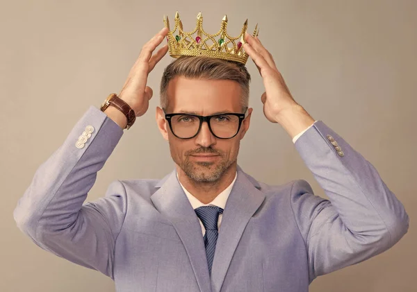 grizzled guy wearing king crown on grey background, success