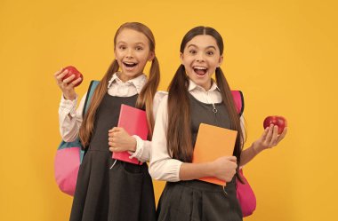 Okul üniformalı mutlu çocuklar okul yemeği yemek için kitap ve elma tutarlar.