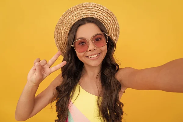 Happy teen girl in summer straw hat and glasses making selfie on yellow background, selfie — Stock Photo, Image