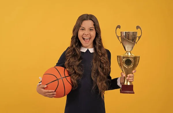 Щаслива дівчина-підліток тримає баскетбол і кубок чемпіона на жовтому фоні, щастя — стокове фото