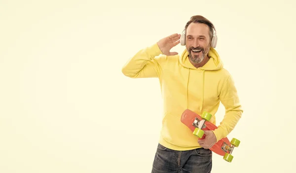 Heureux homme mature skateboarder écouter de la musique portant des écouteurs tenir penny skateboard, streetwise. — Photo