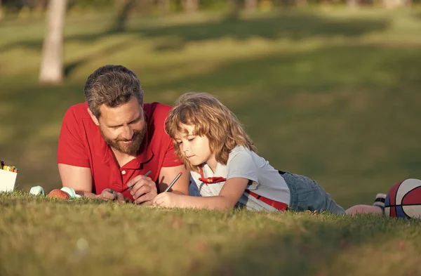 Otec a syn relaxovat na trávě v parku učení kreslit, otcovství — Stock fotografie