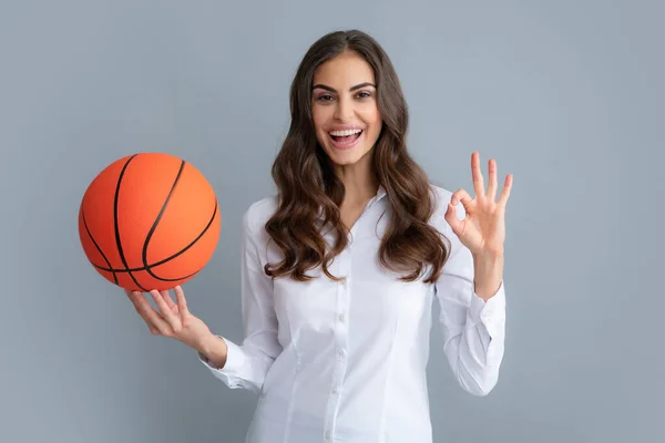 Mujer feliz con signo ok sostener pelota de baloncesto, aislado sobre fondo gris. — Foto de Stock
