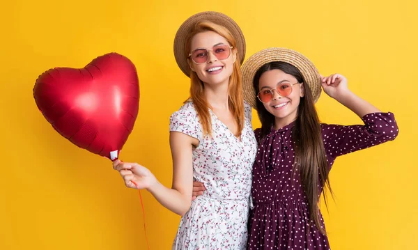 Glad mom and daughter hold love heart balloon on yellow background — стоковое фото