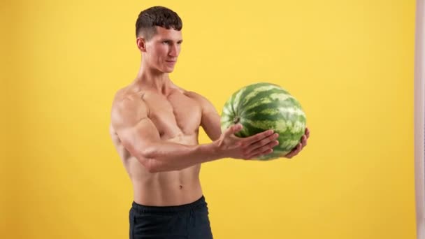 Athlete sportsman lifting heavy watermelon for triceps muscles on yellow backdrop, aspiration — Stock video