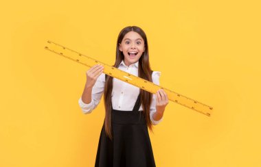 Okul üniformalı hayret bir çocuk matematik kurallarını ölçmek için elinde tutuyor.