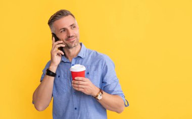 Sarı arka planda kahve fincanı ile telefonda konuşan gülümseyen olgun adam, kopyalama alanı, iletişim