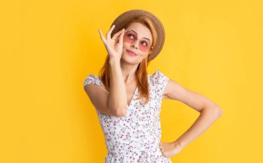 Sarı arka planda hasır şapkalı ve güneş gözlüklü neşeli kadın.