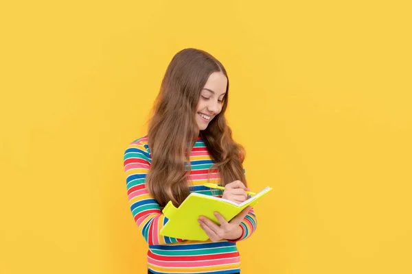 Happy girl dziecko zapisać w copybook żółty tle, umiejętności czytania i pisania — Zdjęcie stockowe