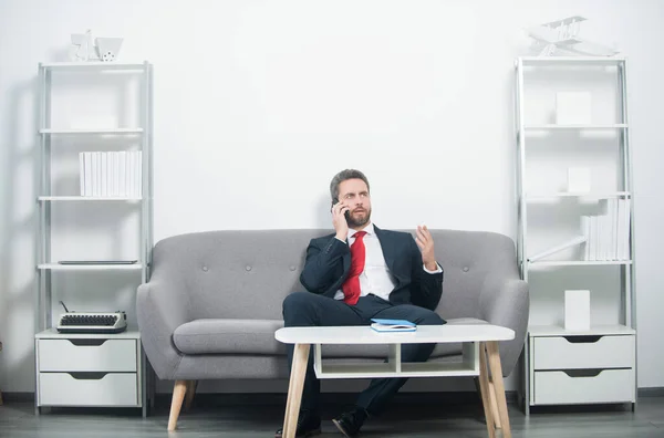Businessman sitting in office and talking on phone — Stock Photo, Image