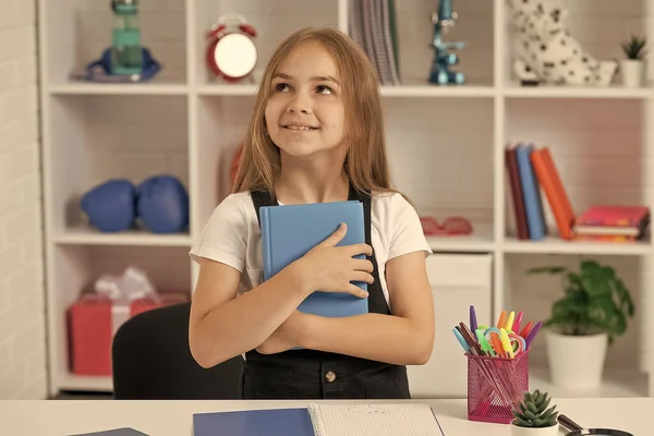 Dreamy kid hold book at school lesson in classroom wear uniform, dreaming — Zdjęcie stockowe