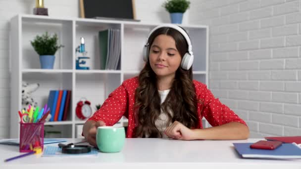 Χαρούμενο έφηβο κορίτσι με ακουστικά πίνοντας τσάι από το κύπελλο, παιδική ηλικία — Αρχείο Βίντεο