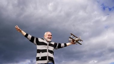 Happy elderly man pretend flying on model aircraft in sky, dream