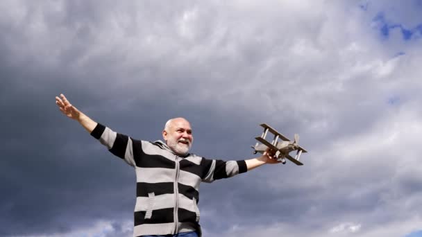 Mutlu yaşlı adam gökyüzünde model bir uçakla uçuyormuş gibi yapıyor, hayal et. — Stok video