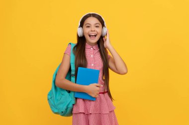 Hayret verici kulaklıklı okul çocuğu sırt çantası, çalışma kitabı ve müzik taşıyor.