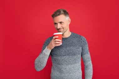 Sabah kahvesi. Kırmızı arka planda sırıtan gri kazaklı adam. Beyaz adam kahve içiyor.