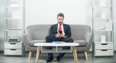 Ofiste oturan işadamı ve telefondaki e-postayı kontrol ediyor