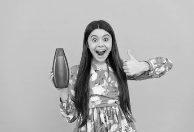 Şaşırmış uzun saçlı çocuk şampuan şişesini tut baş parmağını kaldır, cilt bakımı