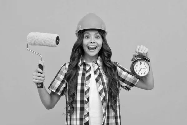 Surprised teen girl hold paint roller and alarm clock. child in helmet. time for decoration. — Stock Photo, Image