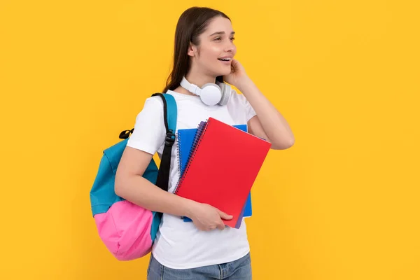 Χαρούμενο νεαρό κορίτσι με σακίδιο και ακουστικά κρατήσει βιβλίο εργασίας σε κίτρινο φόντο, γνώση — Φωτογραφία Αρχείου