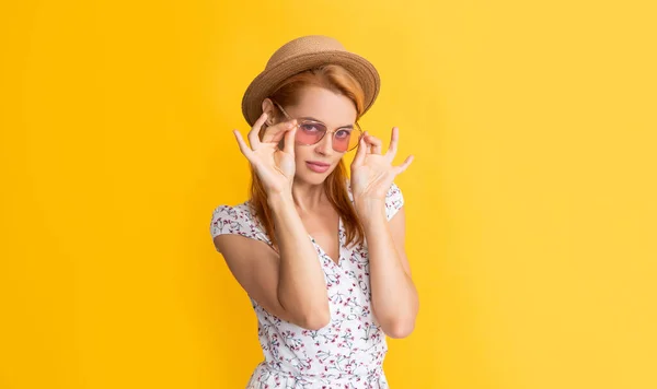 Молода жінка посміхається в солом'яному капелюсі і сонцезахисних окулярах на жовтому фоні — стокове фото