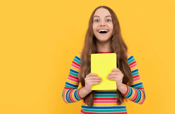 Счастливые девочки улыбаются, держа школьную книгу на желтом фоне, школьное образование — стоковое фото