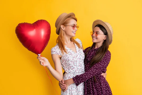 Gülümseyen anne ve kız sarı arka planda aşk balonu tutuyorlar.
